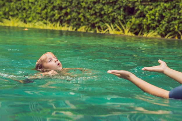 어린이를 위한 여자 수영 강사가 행복한 소년에게 수영장에서 수영하는 법을 가르치고 있습니다
