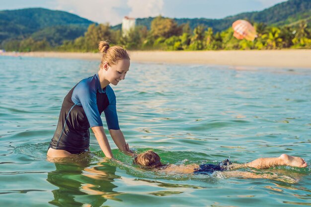 子供のための女性の水泳インストラクターは海で泳ぐために幸せな男の子を教えています