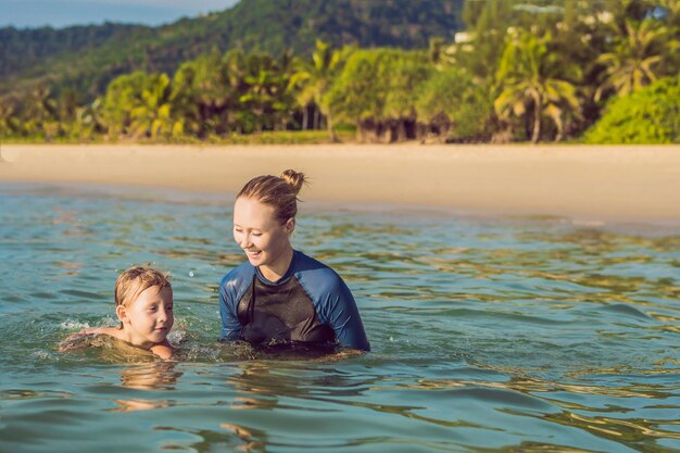 子供のための女性の水泳インストラクターは海で泳ぐために幸せな男の子を教えています