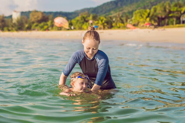 Woman swimming instructor for children is teaching a happy boy to swim in the sea