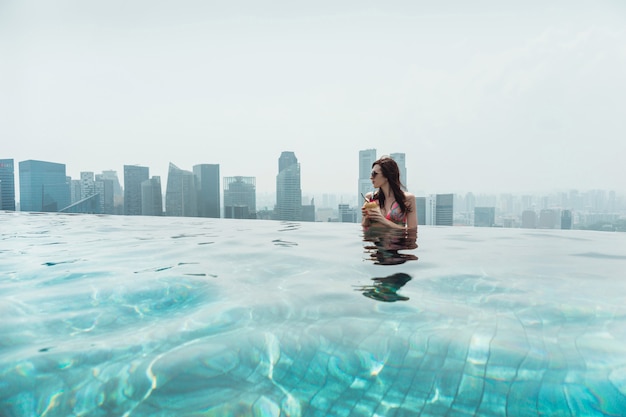 Foto donna che nuota nella piscina all'aperto sul tetto a singapore.una giovane donna con una noce di cocco in mano è rilassante nella piscina all'aperto sul tetto