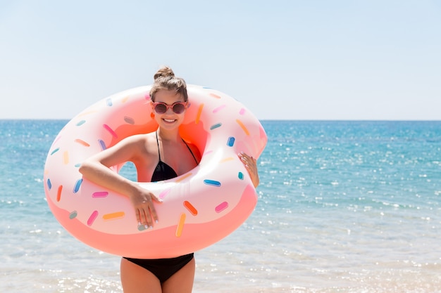 여름 화창한 날에 해변에서 풍선 도넛과 함께 수영하는 여자. 여름 방학 및 휴가 개념.