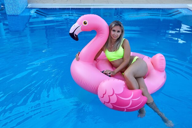 Woman swims in the pool hugging an inflatable pink flamingo toy