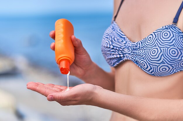 La donna in un costume da bagno applica la crema del blocchetto del sole durante il prendere il sole dal mare in tempo soleggiato in estate