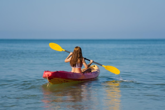 Woman in swimsuit paddling a kayak boat in the sea