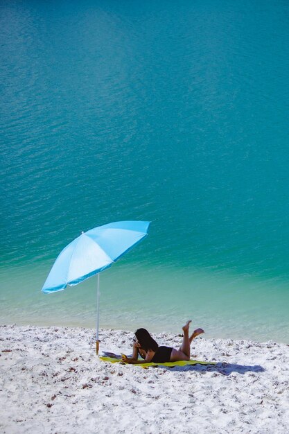 Woman in swimsuit walking by sand beach blue sun umbrella and yellow blanket