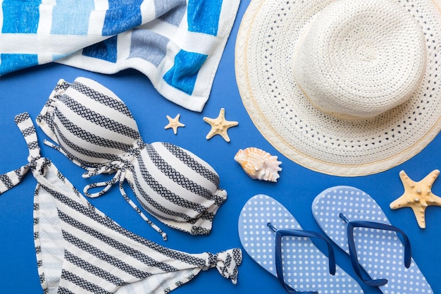 Woman swimwear and beach accessories flat lay top view on colored background Summer travel concept bikini swimsuit straw hat and seasheels Copy space Top view