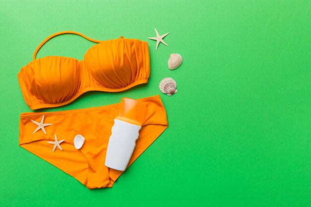 Costumi da bagno donna e accessori da spiaggia vista dall'alto piatta su sfondo colorato concetto di viaggio estivo bikini costume da bagno cappello di paglia e conchiglie spazio copia vista dall'alto