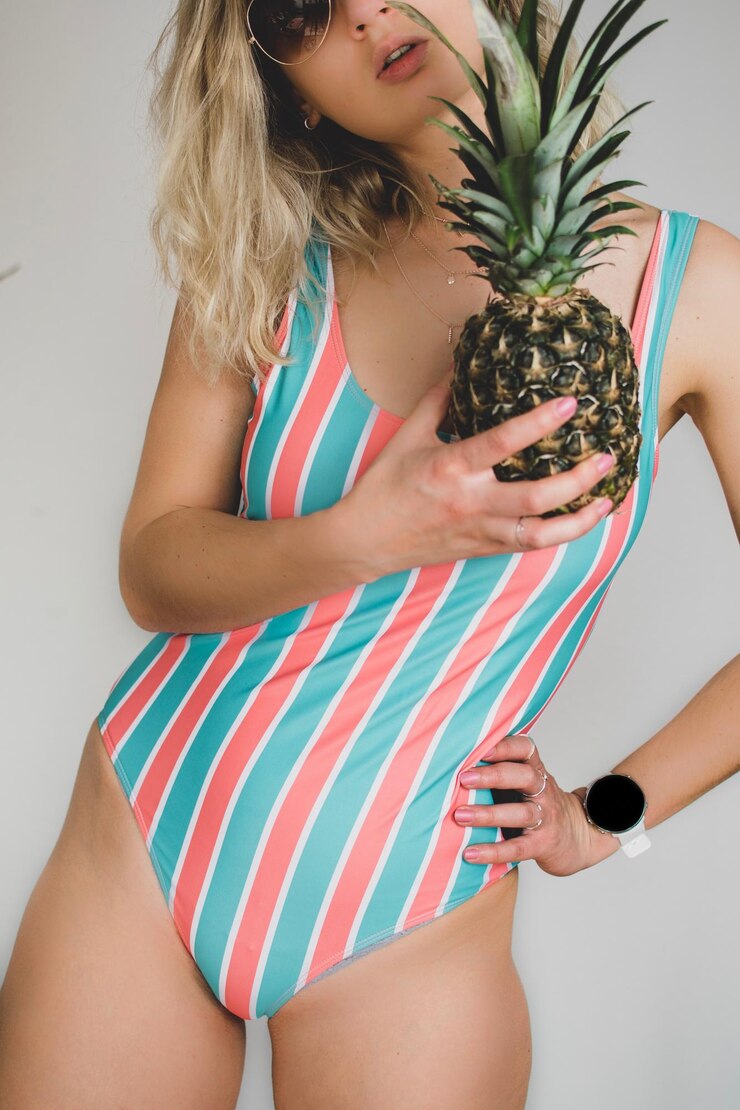 Photo woman in swimwear holding pineapple while standing against white background