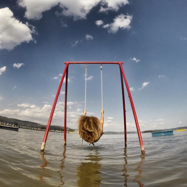 Woman on swing at lake against sky