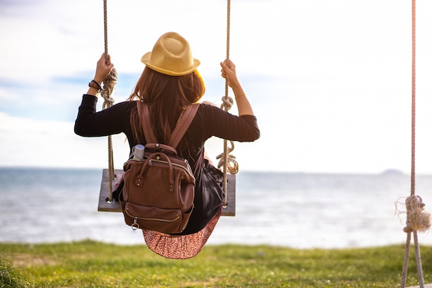 Woman swinging on a wooden swing against the blue sea. Beach holidays on a tropical resort, concept of freedom.