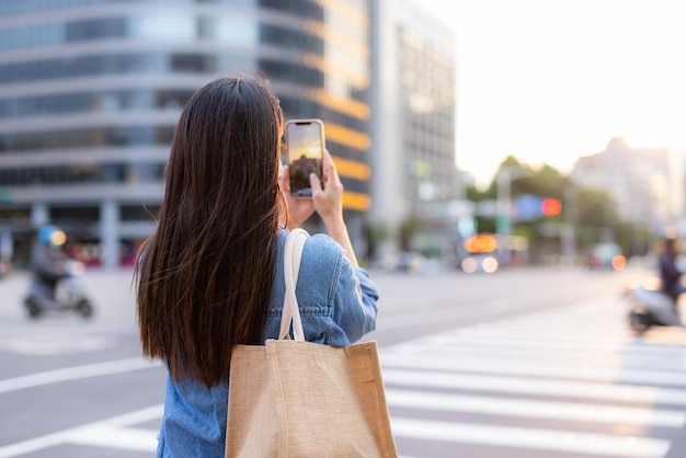 夕暮れの街で女性が携帯電話で写真を撮る