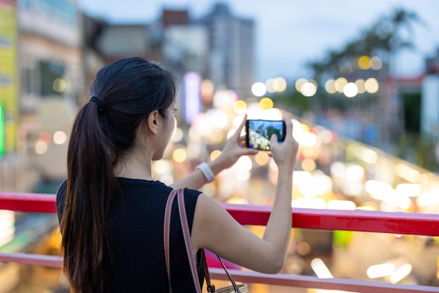 Женщина фотографируется на мобильном телефоне на уличном рынке