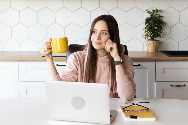 La donna si prende una pausa dal lavoro e beve il tè, lavora online su un laptop