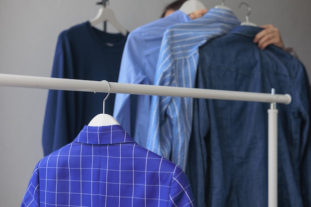 여자는 옷을 보관하거나 쇼핑을 하는 파란색 재킷 셔츠 옷장으로 옷걸이를 가져갑니다.