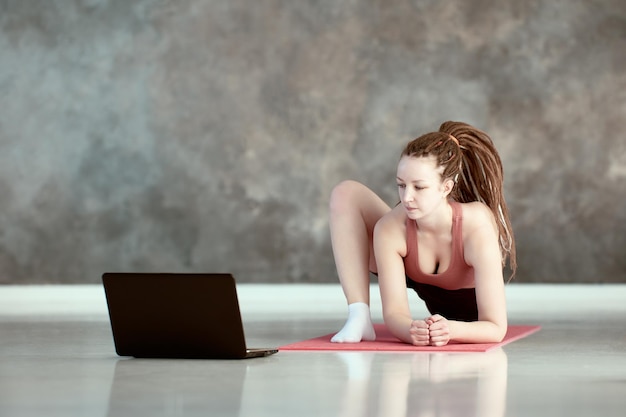 Woman takes online yoga asana lessons using laptop