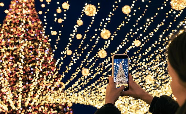 Una donna scatta foto di un albero di natale festivo urbano alto sullo smartphone
