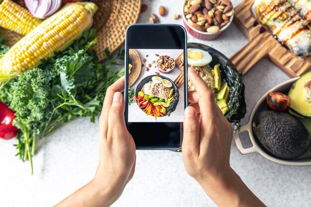 Photo a woman takes a photo of a vegetable bowl on her smartphone