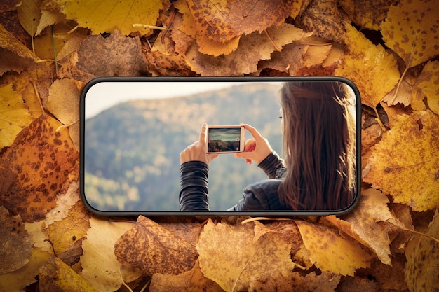 A woman takes pictures of nature and autumn mountains on her smartphone view from the mobile phone screen on the background of autumn leaves social networks travel amospheric mood