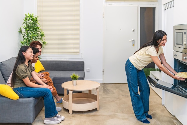 A woman takes pizza out of the oven as friends watch eagerly from the couch