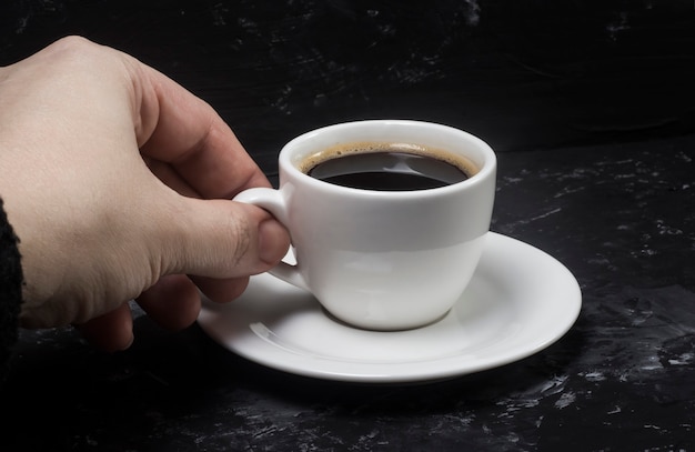 한 여성이 손에 검은 향이 나는 커피와 함께 흰색 컵을 가져다 그 맛을 즐깁니다.