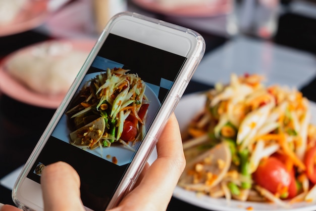スマートフォンでタイのグリーンパパイヤサラダの写真を撮る女性