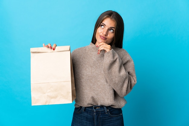 Donna che prende un sacchetto di cibo da asporto isolato su sfondo blu e alzando lo sguardo