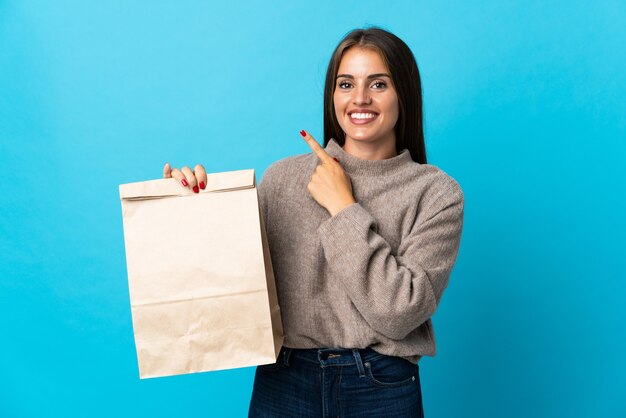 製品を提示するために側面を指している青で隔離の持ち帰り用食品の袋を取っている女性