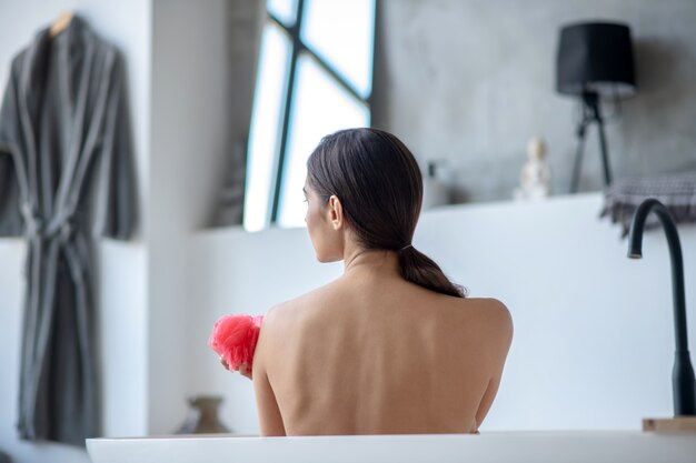 Woman taking a bath with a red sponge