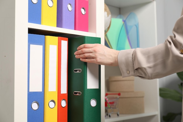 woman taking binder office folder from shelving unit indoors closeup