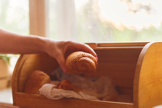 Woman taking a bread loaf from a bread box in the kitchen at home