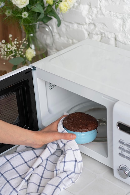 Woman taking chocolate mugcake out of microwave oven closeup Vertical image