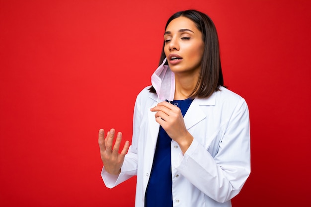 Photo woman taking off virus protective mask on face against coronavirus and white medical coat