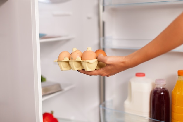 Woman taking out eggs from fridge in the morning for breakfast. Housewife getting helthy eggs and other ingredients from refrigerator in her kitchen.