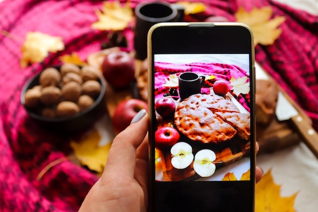 Foto donna che prende foto della torta di mele sul telefono cellulare atmosfera autunnale messa a fuoco selettiva