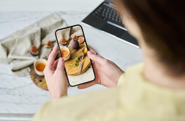携帯電話で料理の写真を撮る女性