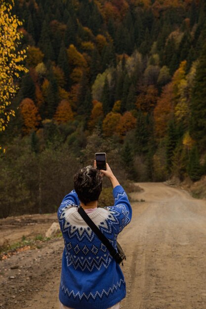 山と秋の森の秋の色の彼女のスマートフォンで写真を撮る女性