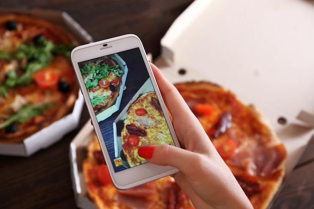 Photo woman taking a photo of pizza with the smartphone