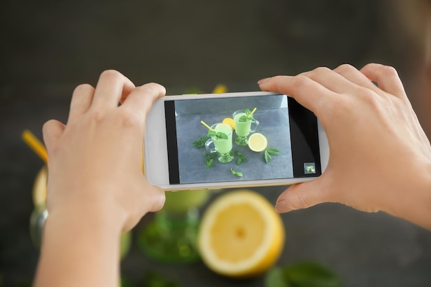 Woman taking photo of smoothies with smart phone in studio Concept of food photography