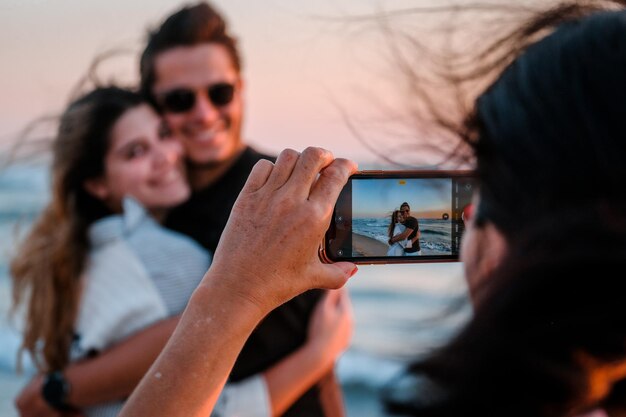 Photo woman taking a photo of two young adults using a mobile phone