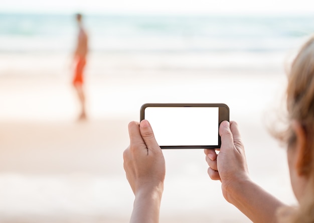 woman taking picture by smartphone at beach