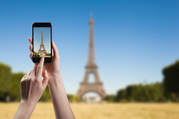 Woman taking a picture of of Eiffel tower, view from Champ de Mars in the morning with a blue sky in a background