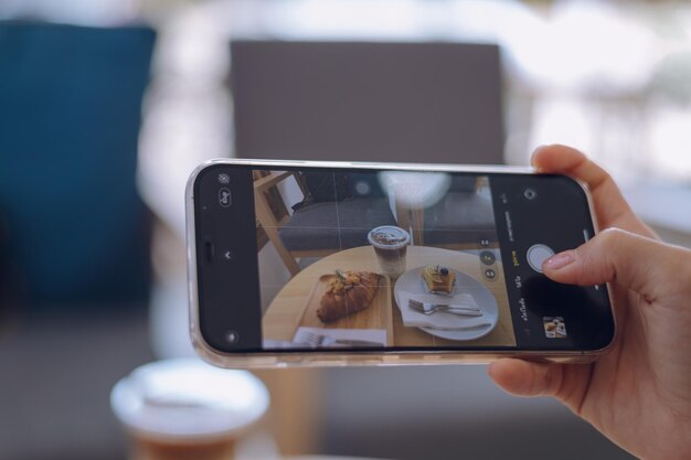 Foto donna che scatta una foto di cibo con un telefono cellulare in un bar