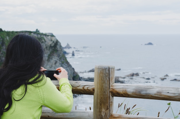 Foto donna che cattura le immagini con il telefono cellulare di un paesaggio marittimo.