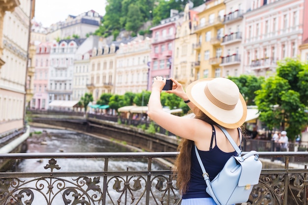 スマートフォンで写真を撮る女性。屋外でカメラと帽子のスタイリッシュな夏の旅行者の女性