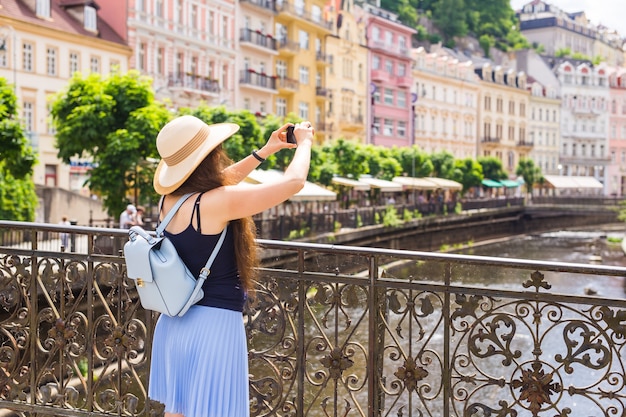 Фото Женщина фотографирует со смартфоном стильный летний путешественник женщина в шляпе с камерой на открытом воздухе в