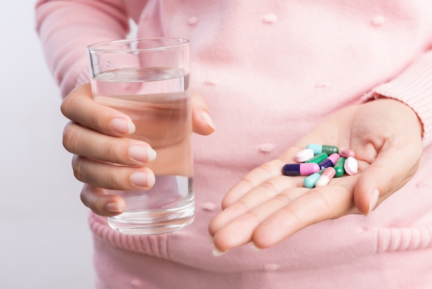 Woman taking in pill and another hand holding a glass of clean mineral water.