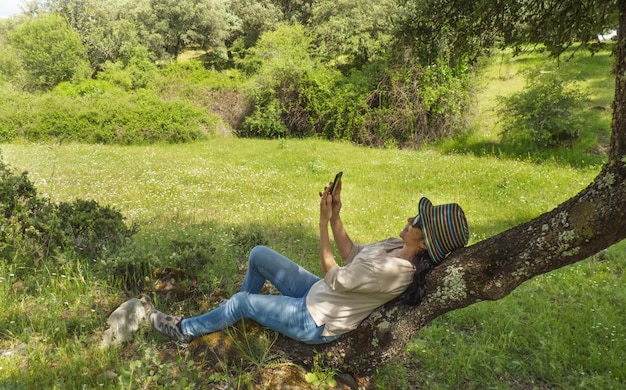 Foto donna che si fa un selfie con il telefono su un albero a terra