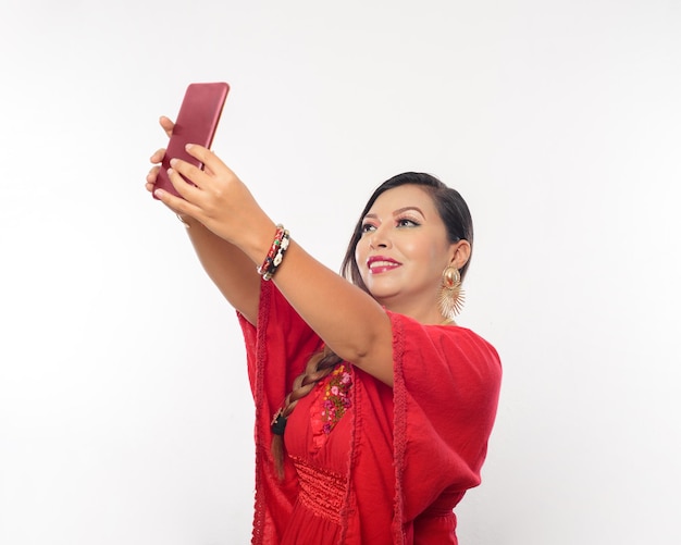 Woman taking a selfie. Mexican woman wearing embroidered blouse taking a selfie. White background.