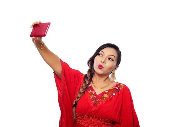 Woman taking a selfie. Mexican woman wearing embroidered blouse taking a selfie. White background.